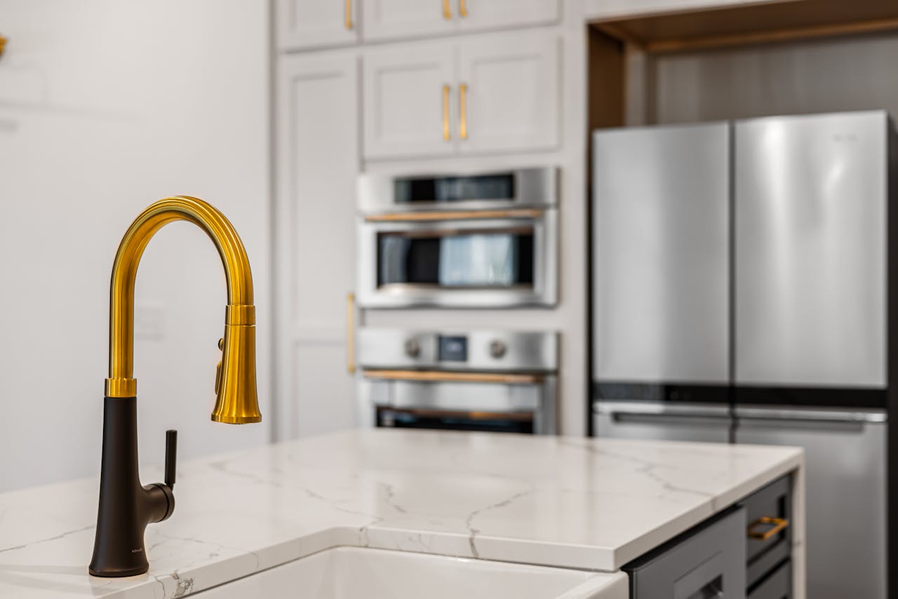 Elegant kitchen interior with a modern gold faucet and sleek stainless steel appliances.