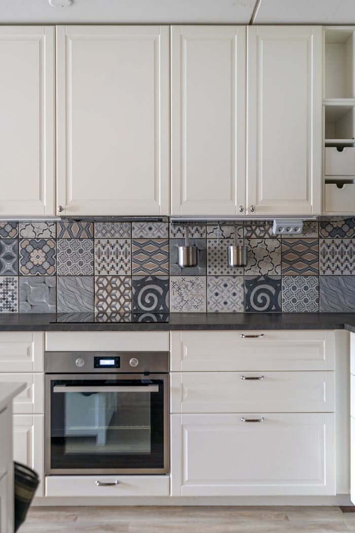 Elegant kitchen design featuring white cabinets and a patterned mosaic tile backsplash.